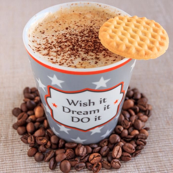Motivational coffee mug with frothy cappuccino, surrounded by coffee beans and topped with a cookie. Perfect cozy morning.