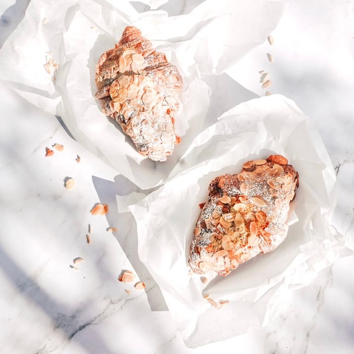 pexels-photo-13439695-13439695 Top view of two almond croissants on white paper, dusted with sugar and almonds, on a sunny day.