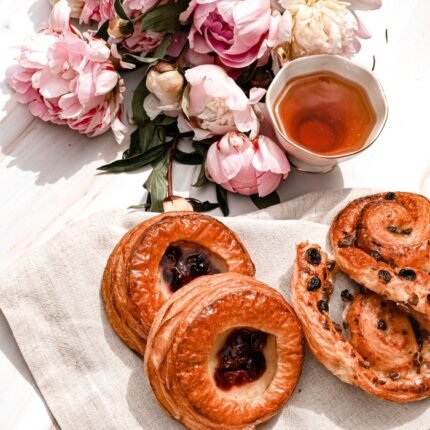High-angle view of pastries and tea with pink peony flowers in a bright setting.
