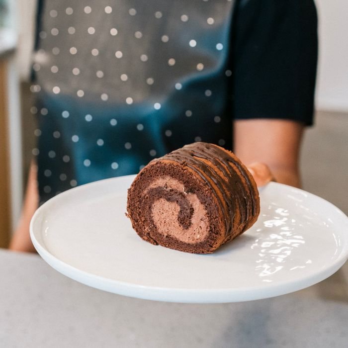 Close-up of a chocolate Swiss roll on a white plate being held by a person.