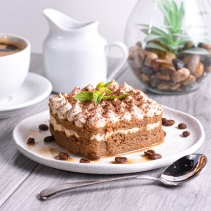 Tiramisu cake with cream topping, garnished with mint and coffee beans.