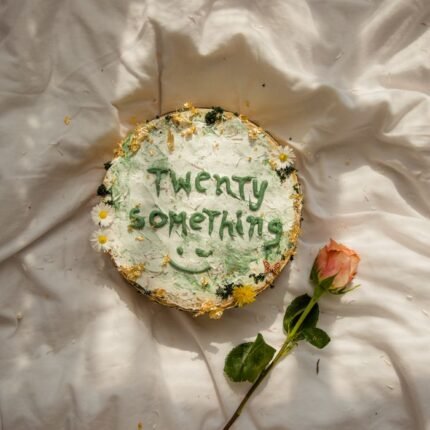 Artistic cake decoration with 'Twenty Something' and a rose on a white cloth backdrop.