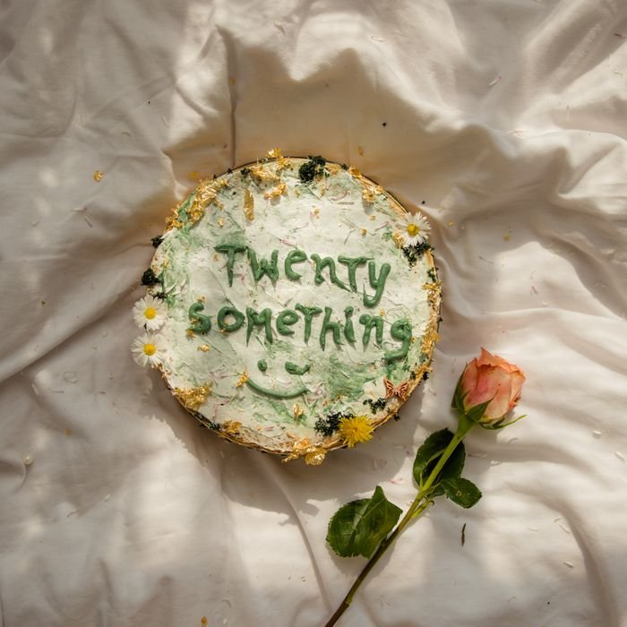 Artistic cake decoration with 'Twenty Something' and a rose on a white cloth backdrop.