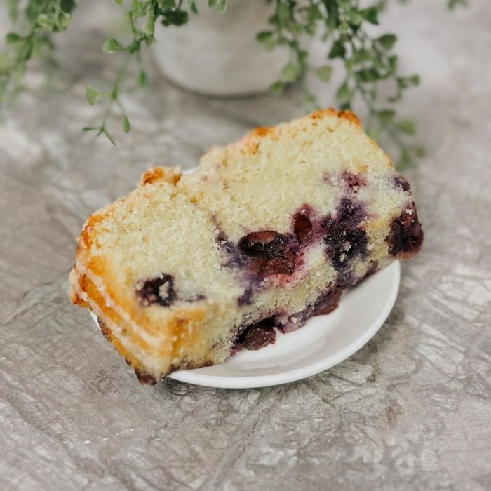 pexels-photo-31430609-31430609 Slice of homemade blueberry loaf cake on white plate with greenery background.