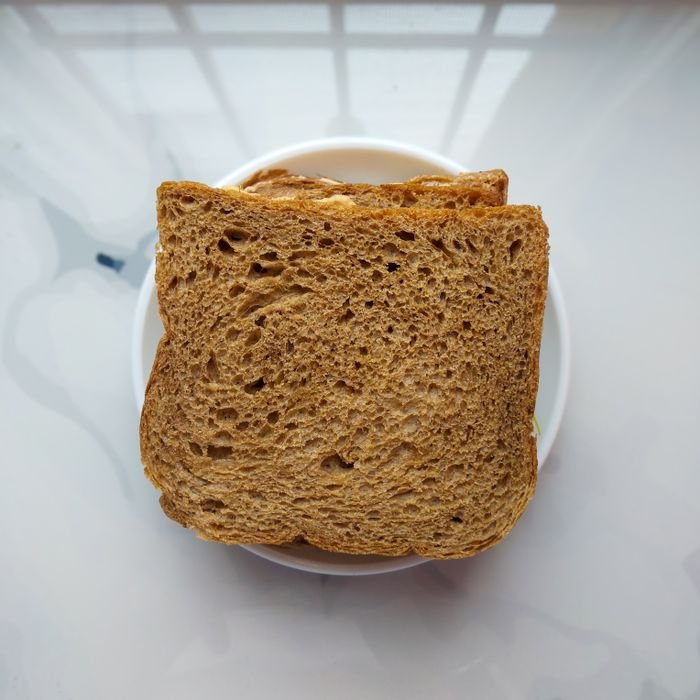 Top view of fresh, rustic brown bread slices on a white plate indoors.