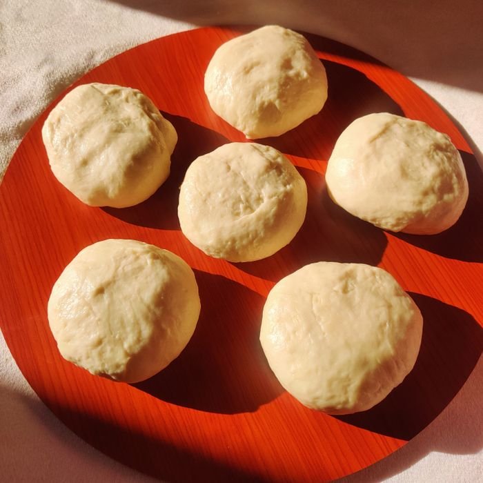 Six freshly prepared dough balls on a vibrant red plate, bathed in warm sunlight.