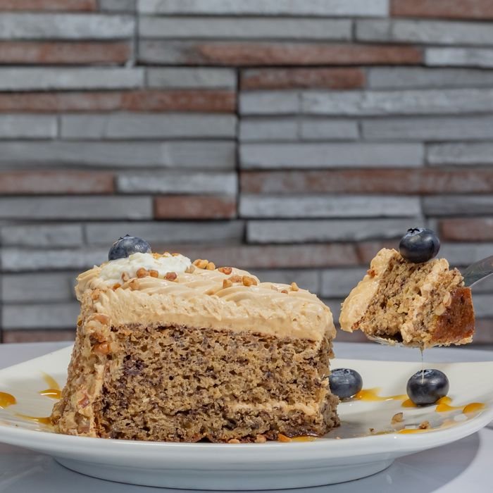 A slice of banana cake with caramel and pecans, garnished with blueberries, on a white plate.