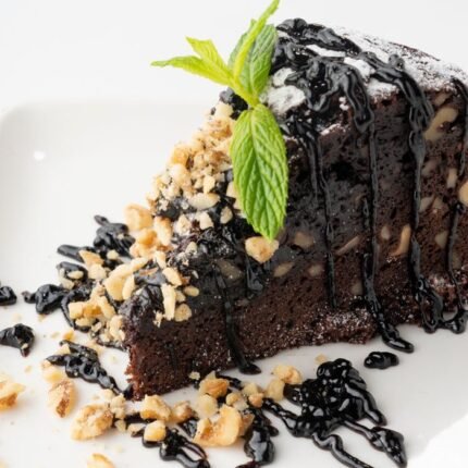 Rich chocolate cake slice topped with mint and nuts, drizzled with chocolate syrup.