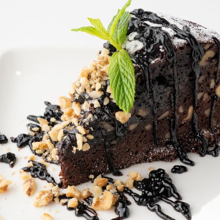 Rich chocolate cake slice topped with mint and nuts, drizzled with chocolate syrup.