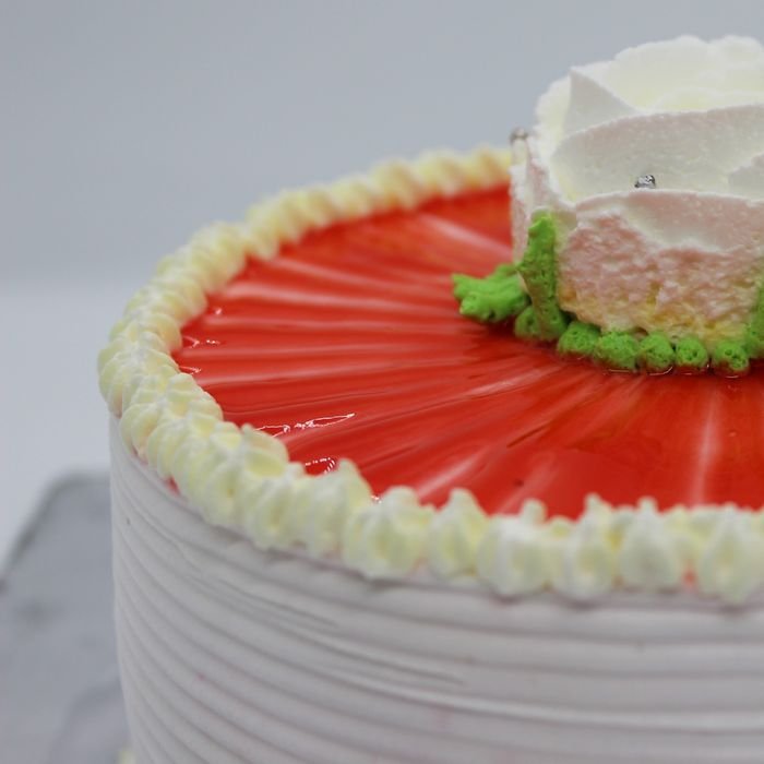 Close-up of a beautifully decorated cake with a strawberry glaze and cream flower on top.