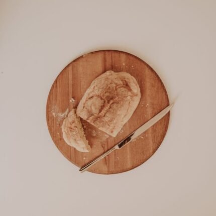 A loaf of rustic bread partially sliced on a round wooden board, accompanied by a knife.