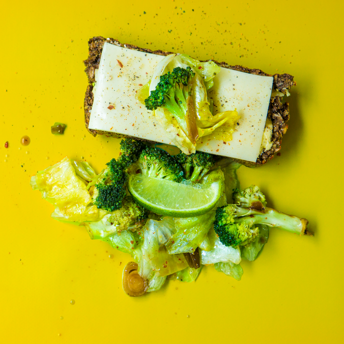 Delicious broccoli salad with cheese and lime on rye bread, set against a vibrant yellow backdrop.