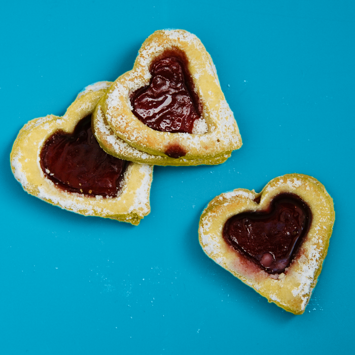 Delicious heart-shaped cookies with jam filling on a vibrant blue background.