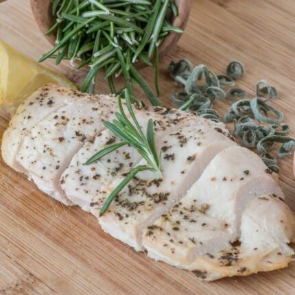 Sliced chicken breast with lemon and rosemary on a wooden board.