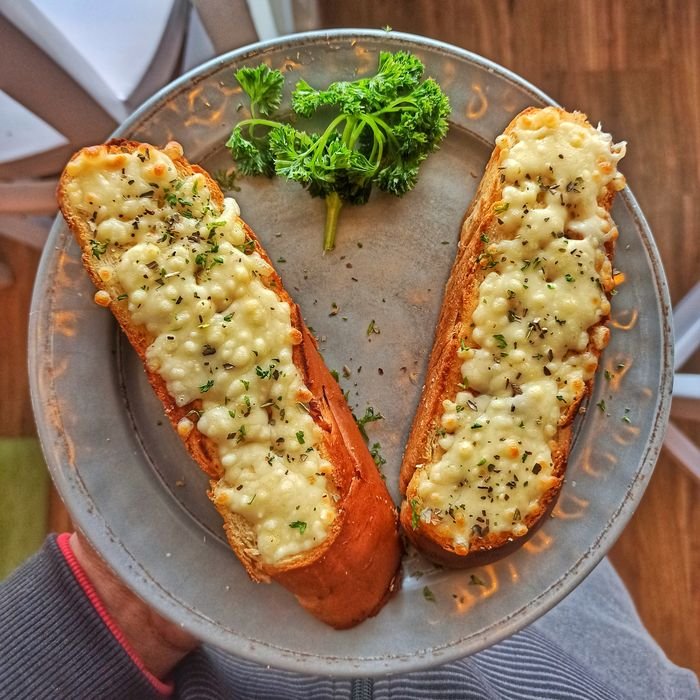 Appetizing garlic bread with melted cheese on a ceramic plate, garnished with parsley, in a still life setting.